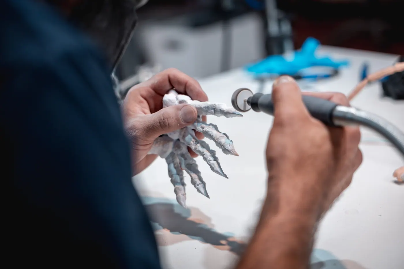 Manos de un técnico puliendo con una herramienta rotativa la réplica de una garra de dinosaurio
