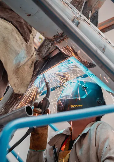 Soldador con máscara trabajando sobre la estructura metálica de un montaje, entre chispas